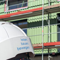 Bauhelm mit Aufdruck "leben bauen bewegen" vor einem eingerüsteten Gebäude